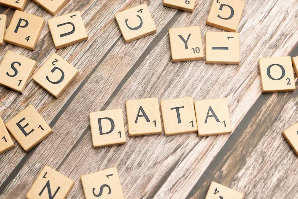 Wooden tiles spelling out the word DATA, scattered among other letter tiles on a plank surface.