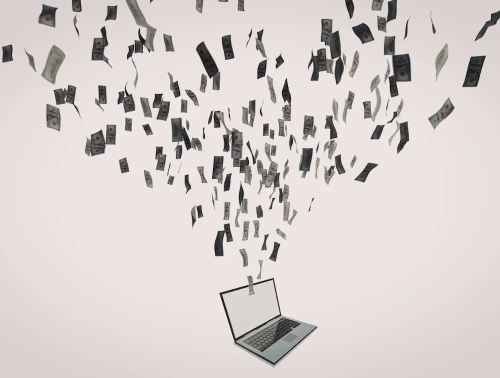 Cash flying out of an open laptop, illustrating the cost of unmanaged duplicate records.