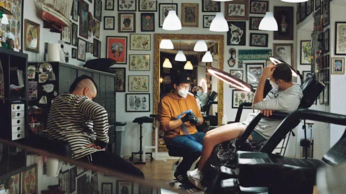 A client getting a tattoo in a studio with walls covered in tattoo flash art, the kind of beauty and wellness business Booksy serves.