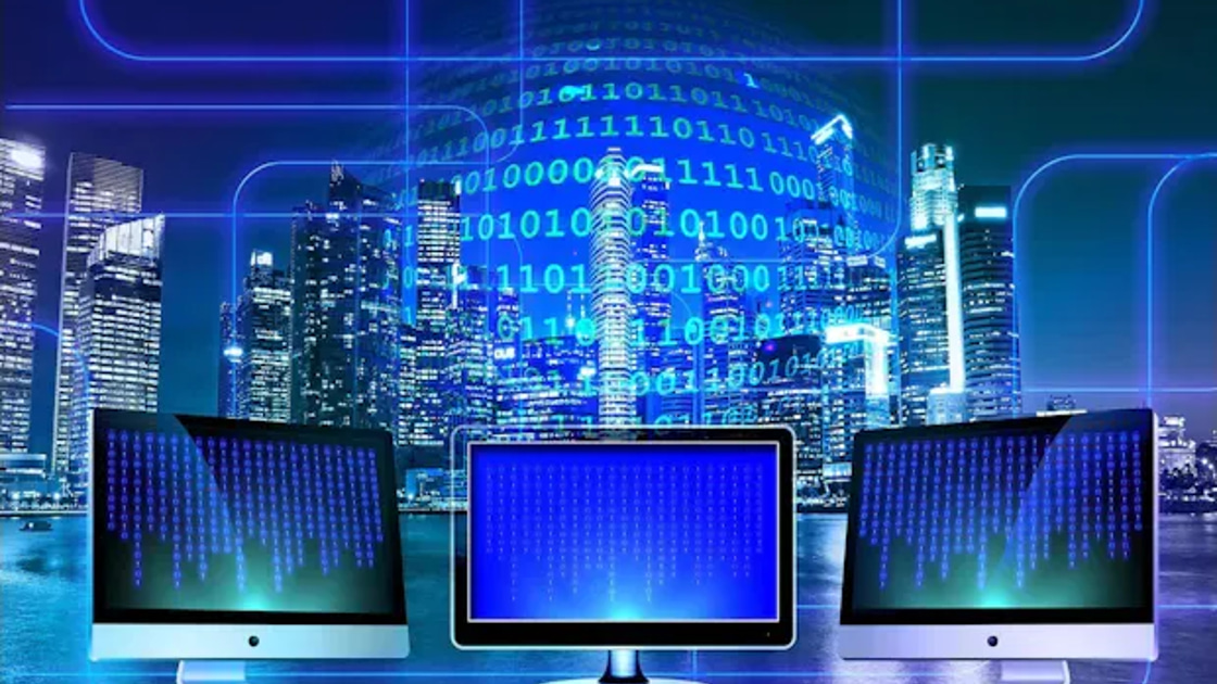 Three computer monitors displaying streams of binary code, set against a city skyline at night with a glowing globe of binary digits overhead.
