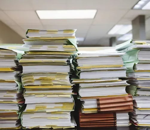 Stacks of paper folders and binders piled on an office desk