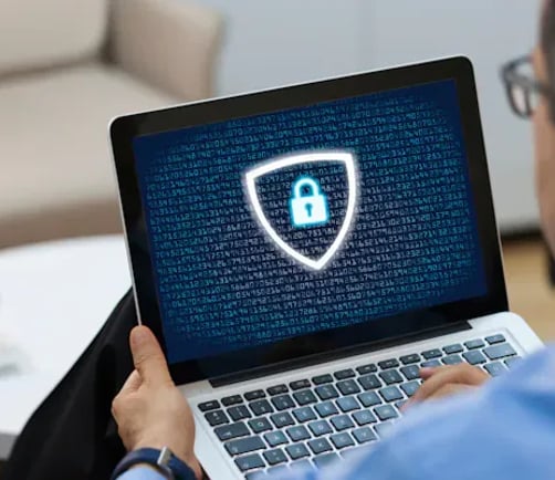 A person holding a laptop that displays a digital security shield and padlock icon
