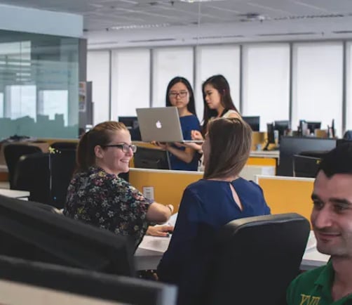 Colleagues reviewing data together at a shared workstation, one holding a laptop.
