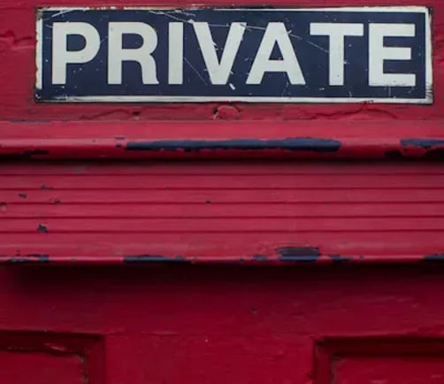 A weathered wooden door painted red, with a small sign reading "Private" mounted above it.