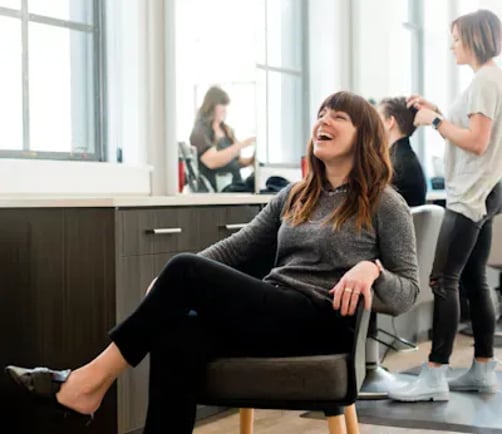 Customer laughing during an appointment at a salon, with staff attending to other clients in the background