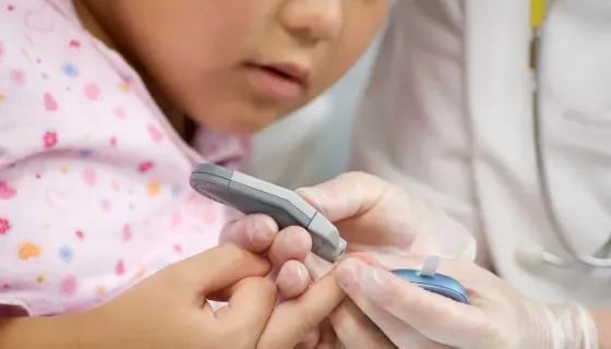 A healthcare worker performing a finger-prick blood glucose test on a child's hand