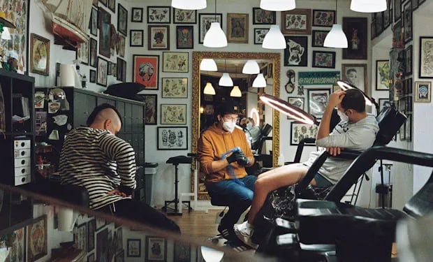 A client getting a tattoo in a studio with walls covered in tattoo flash art, the kind of beauty and wellness business Booksy serves.