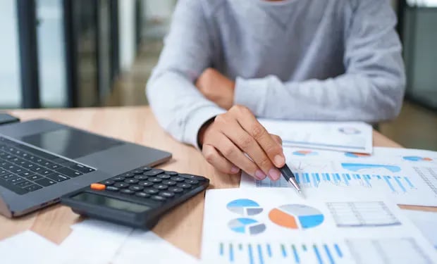 A person reviewing financial charts and budget reports with a calculator and laptop on the desk.